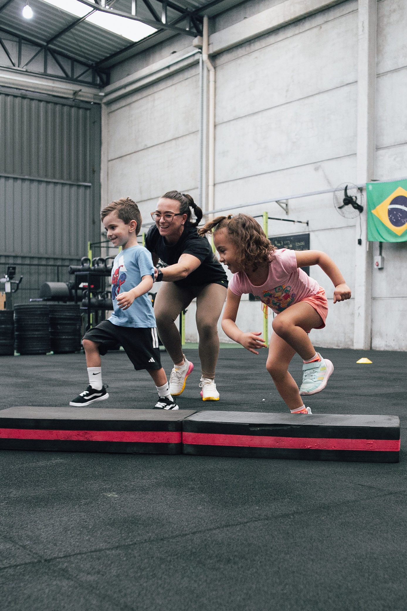 Duas crianças saltando obstáculos com acompanhamento da coach na aula de Cross Kids